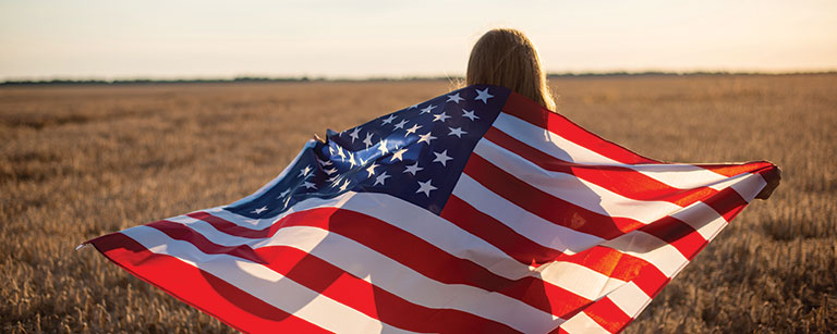 girl standing in field holding United States of America Flag